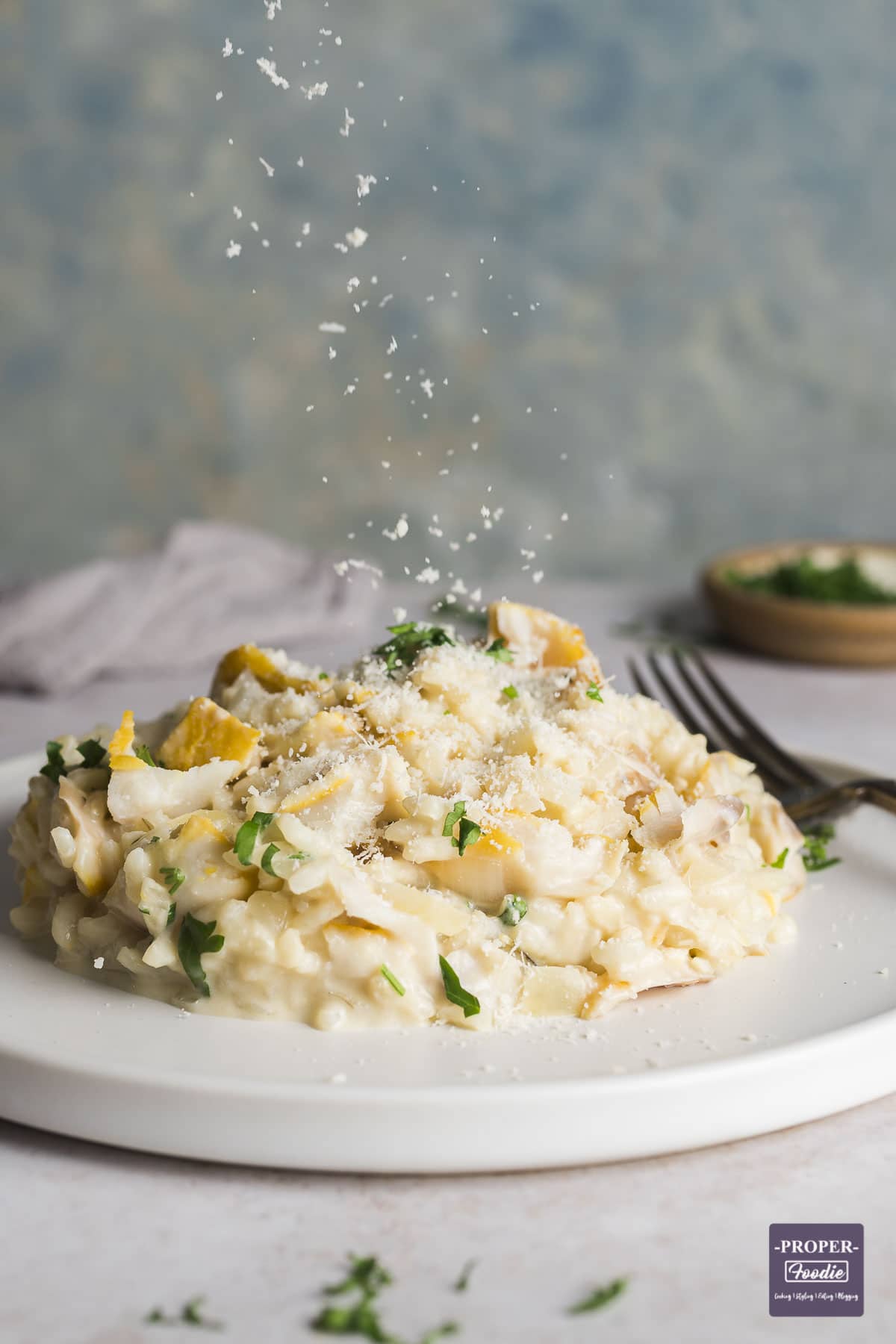 Creamy smoked haddock risotto piled neatly on a small plate, with parmesan being sprinkle on top.