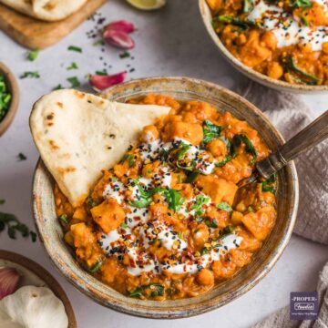 Sweet potato and chickpea curry in a bowl with naan bread and topped with yogurt and coriander.