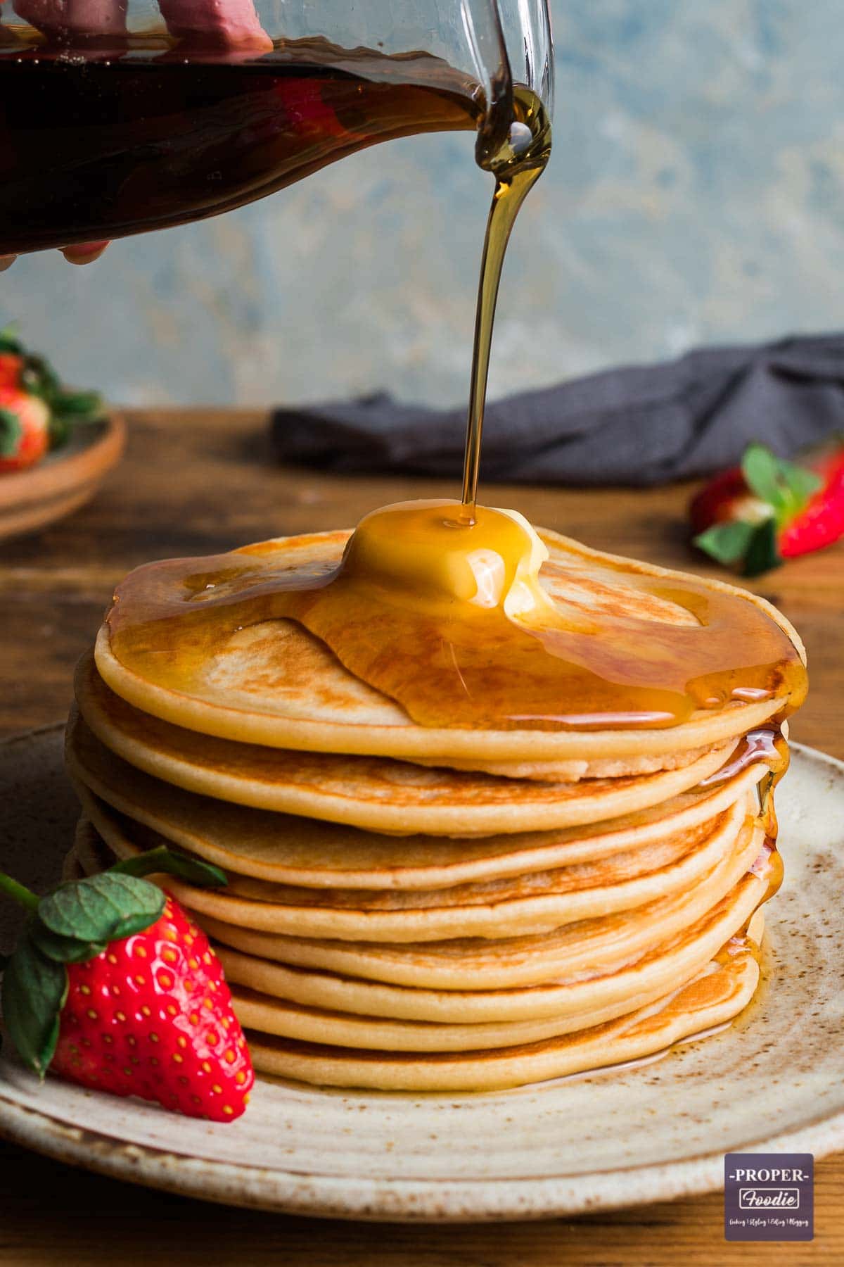 A stack of pancakes with a piece of butter melting on the top and syrup poured over and drizzling down one side.