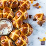 Small hot cross buns arranged in a tear and share style ring with melted chocolate dip at the side.