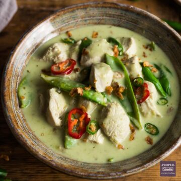 A bowl of Thai green chicken curry with mangetout, green coconut sauce and topped with sliced green chillies and crispy onions.