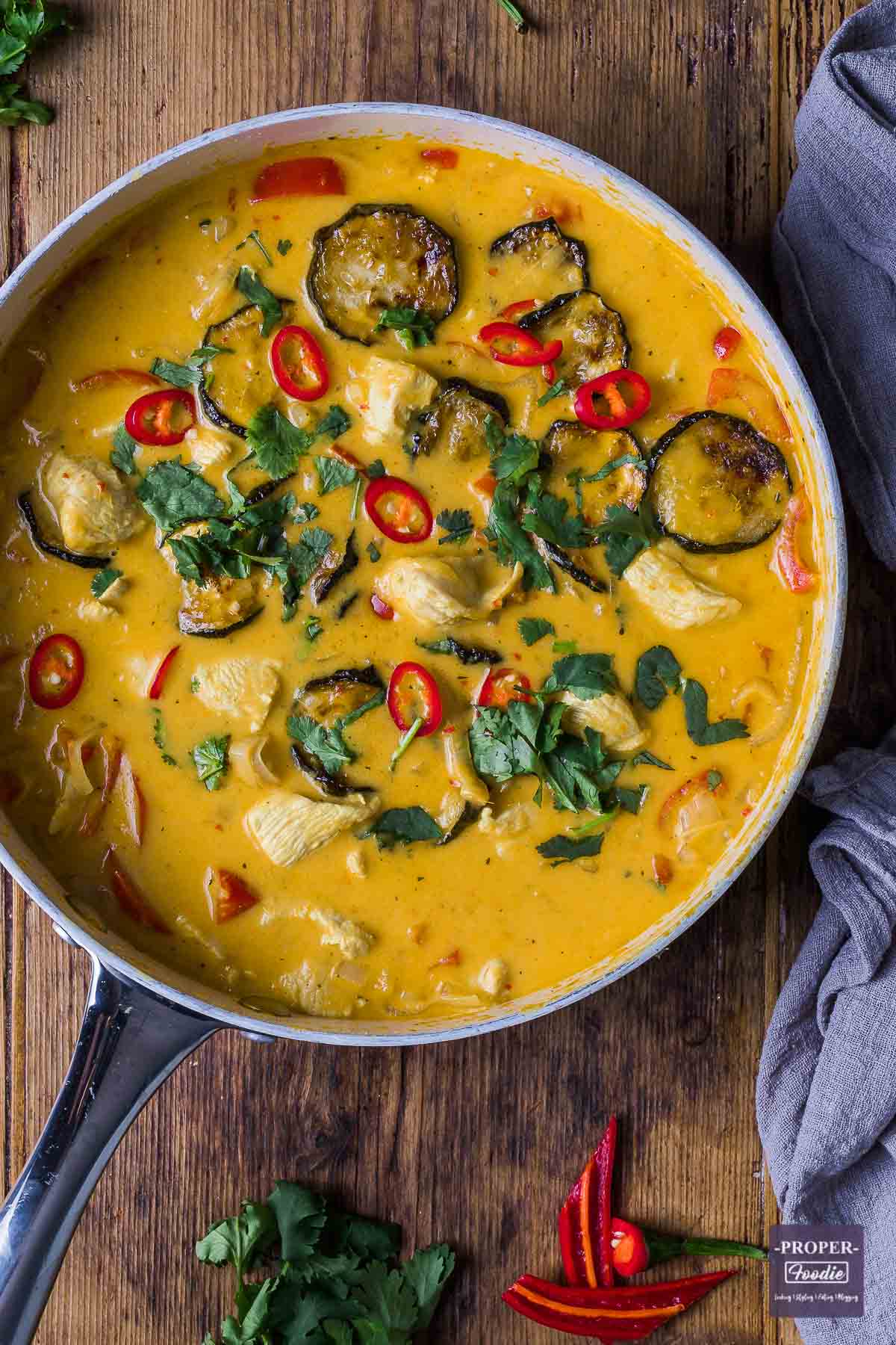 Thai red chicken curry in a large pan topped with sliced red chillies and fresh coriander.