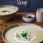 A bowl of leek and potato soup topped with a swirl of cream and chopped chives.