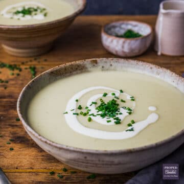 A bowl of leek and potato soup topped with a swirl of cream and chopped chives.