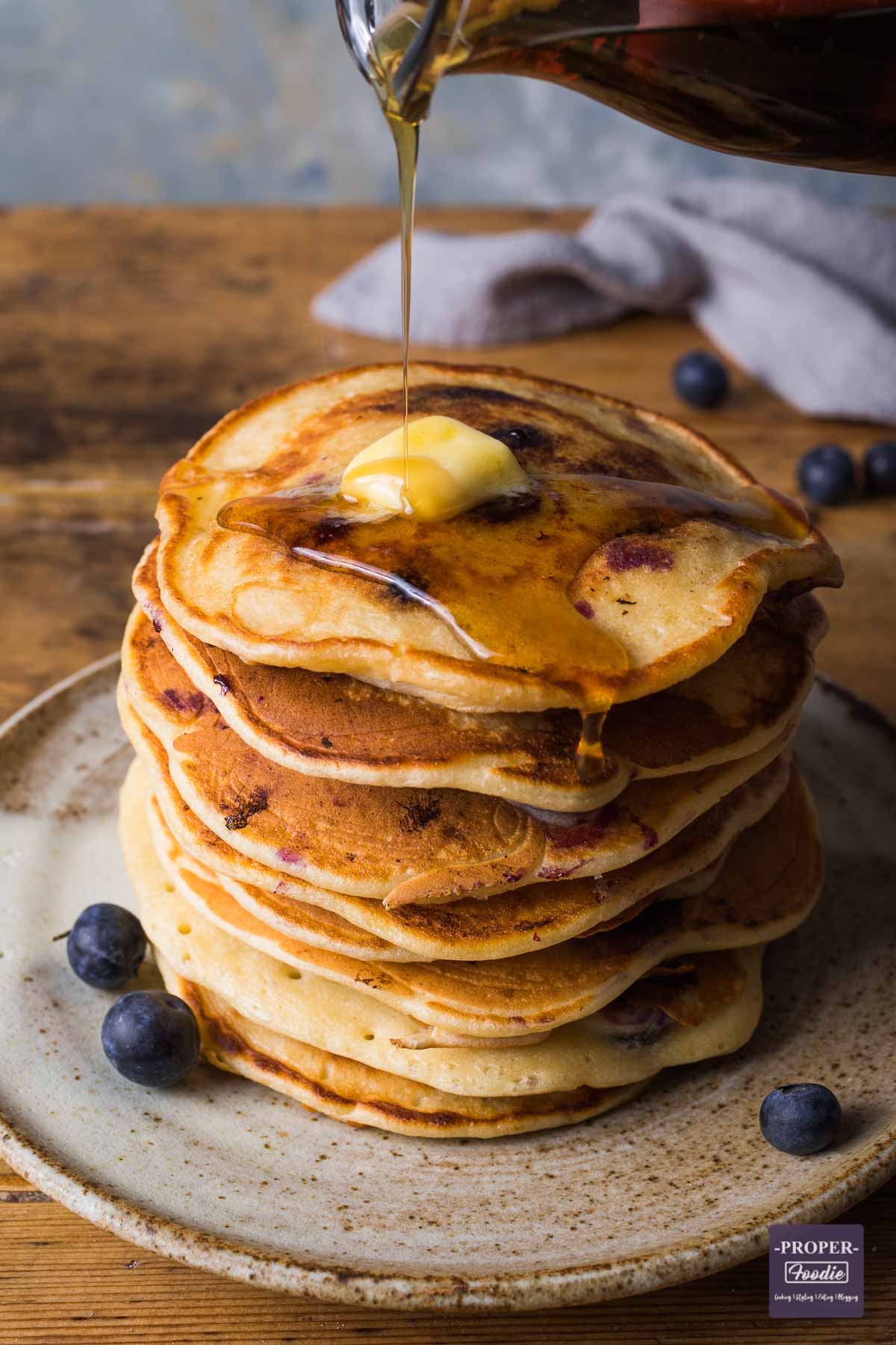 Stack of American style blueberry pancakes with a piece of butter on top and syrup being poured over