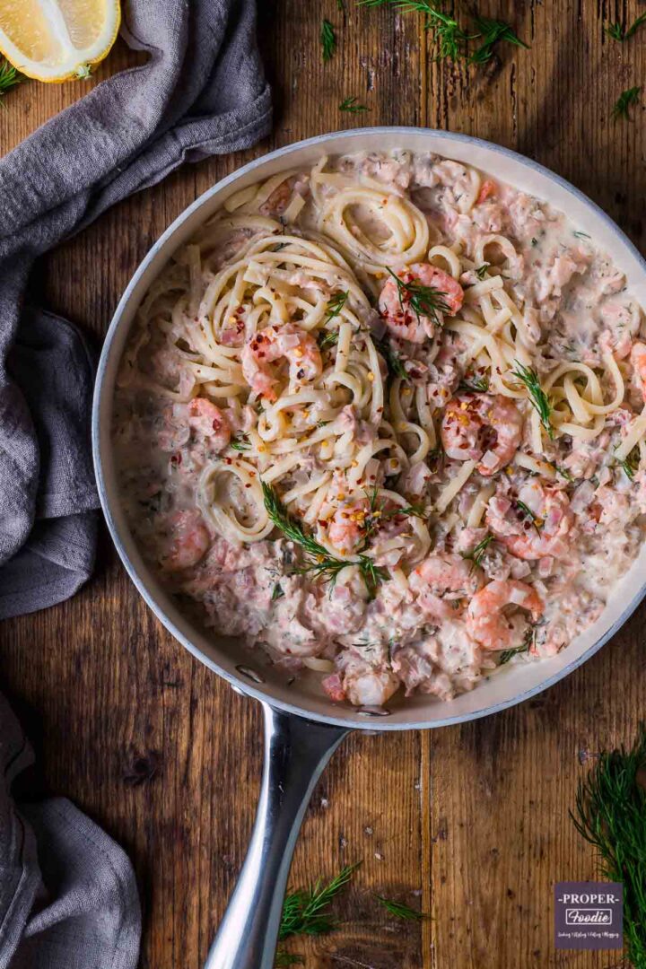 A large shallow pan, viewed from above, filled with salmon and prawn linguine in a creamy sauce and finished with fresh dill and chilli flakes.