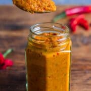 A small jar filled with home Thai red curry paste with teaspoon of paste being held above the jar.