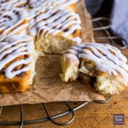 Baked cinnamon swirls stuck together in two side by side rows with icing on the top and one roll broken off with a bite taken.