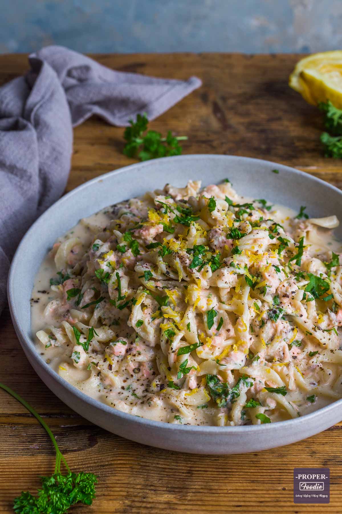 Creamy salmon pasta in a large blue bowl and topped with freshly chopped parsley and lemon zest.