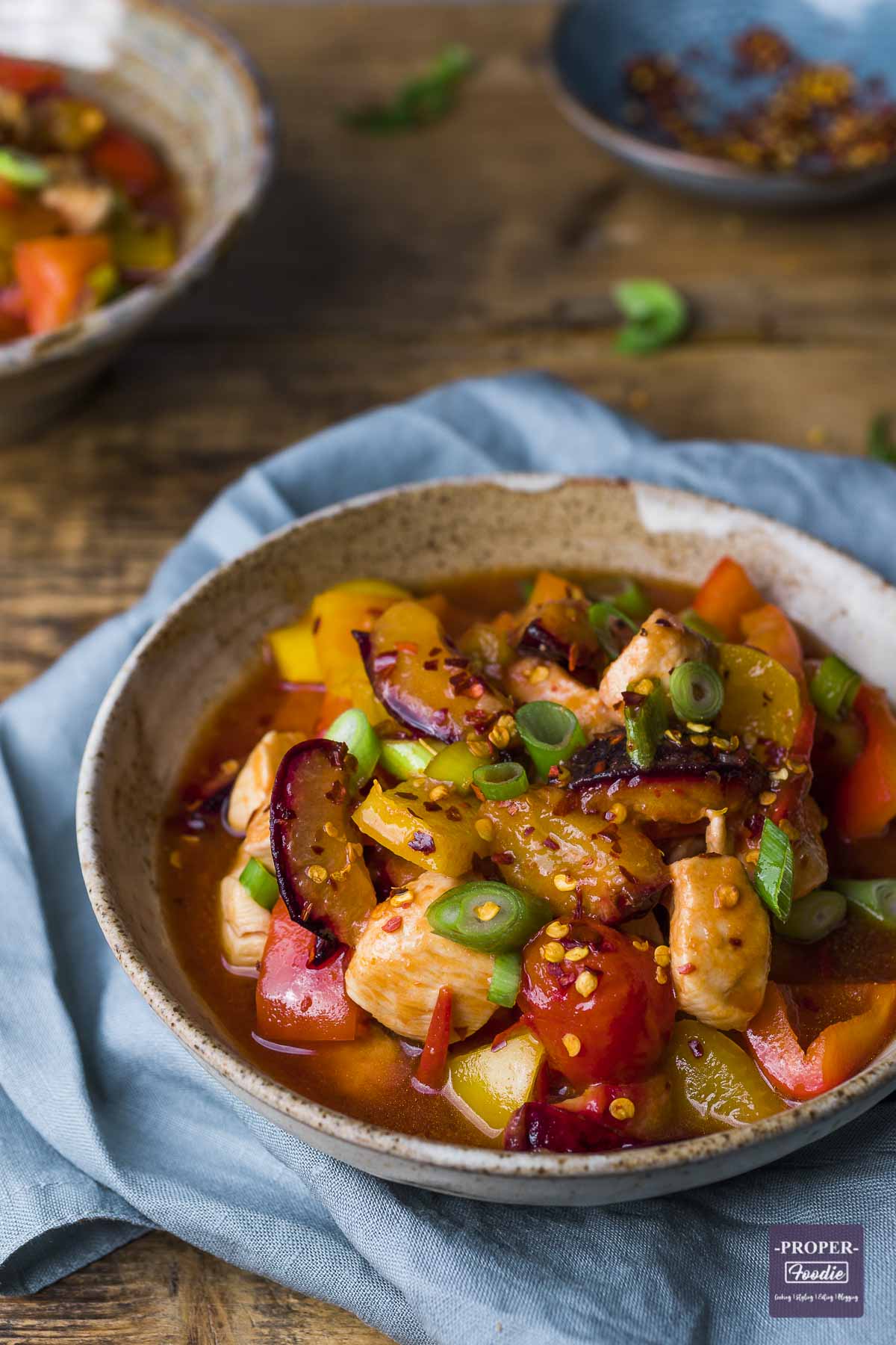 Sweet and sour chicken in a bowl topped with spring onions and chilli flakes.