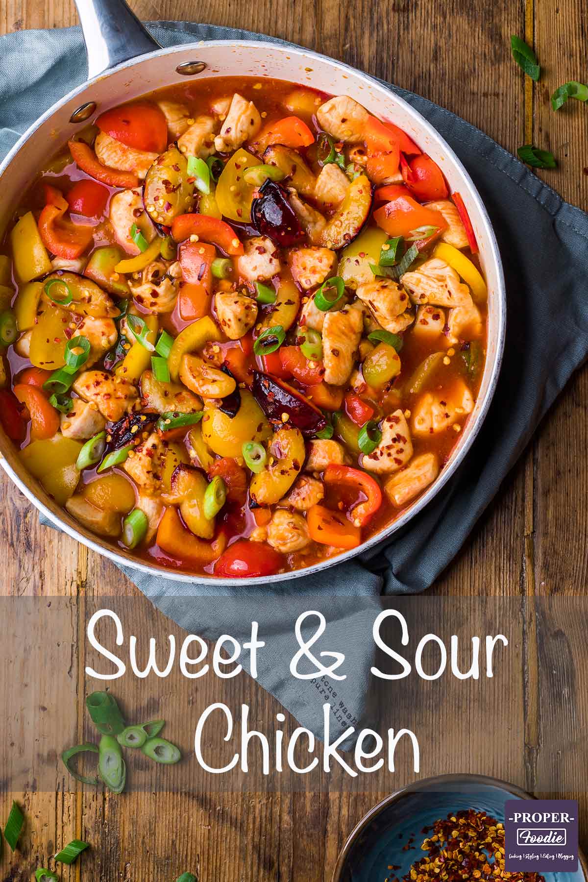 Sweet and sour chicken in a large pan topped with spring onions and chilli flakes.